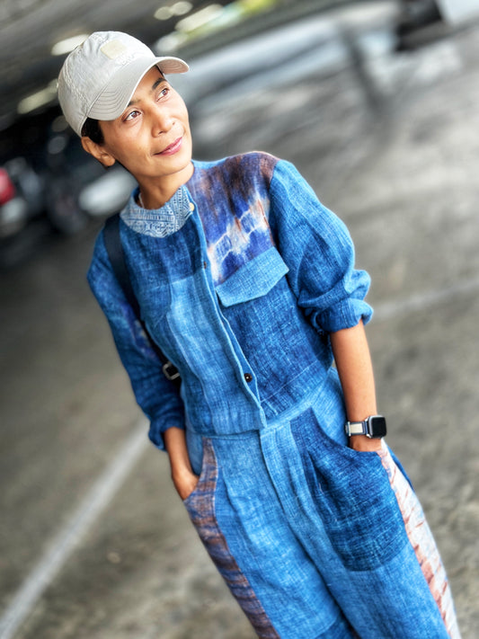 Nuichan patchwork jacket and pants set on a woman, featuring a indigo design with shibori and batik details, against a urban parking garage backdrop, with baseball cap and smartwatch