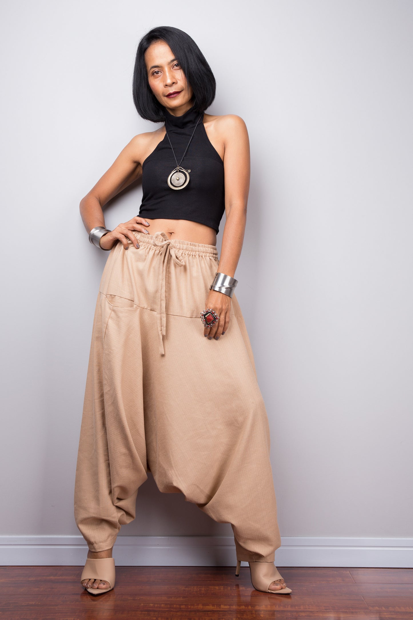 Model wearing beige harem pants with a loose fit, standing against a plain background, showcasing the full-length view.