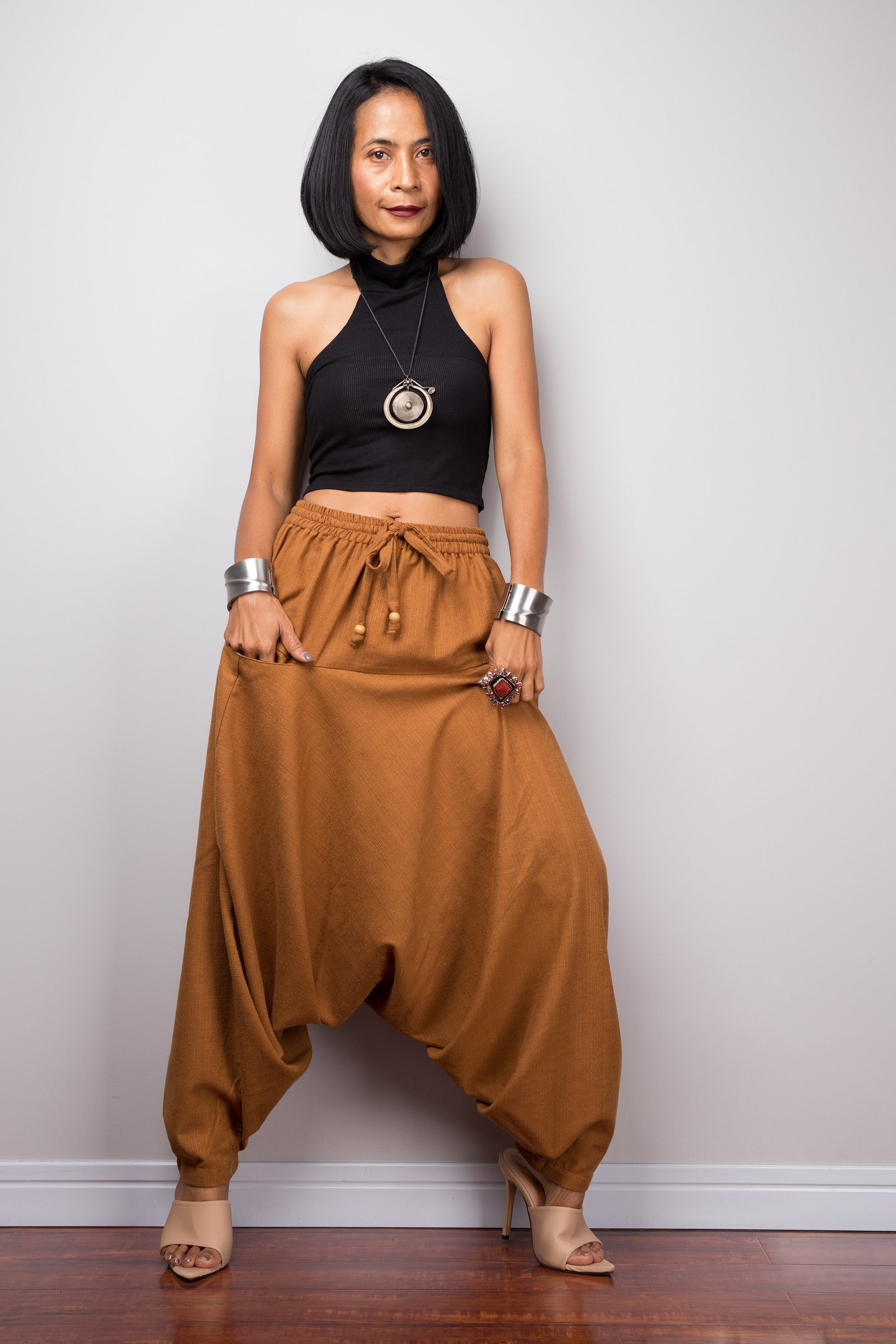 Model wearing brown harem pants with a loose fit, standing against a plain background, showcasing the full-length view