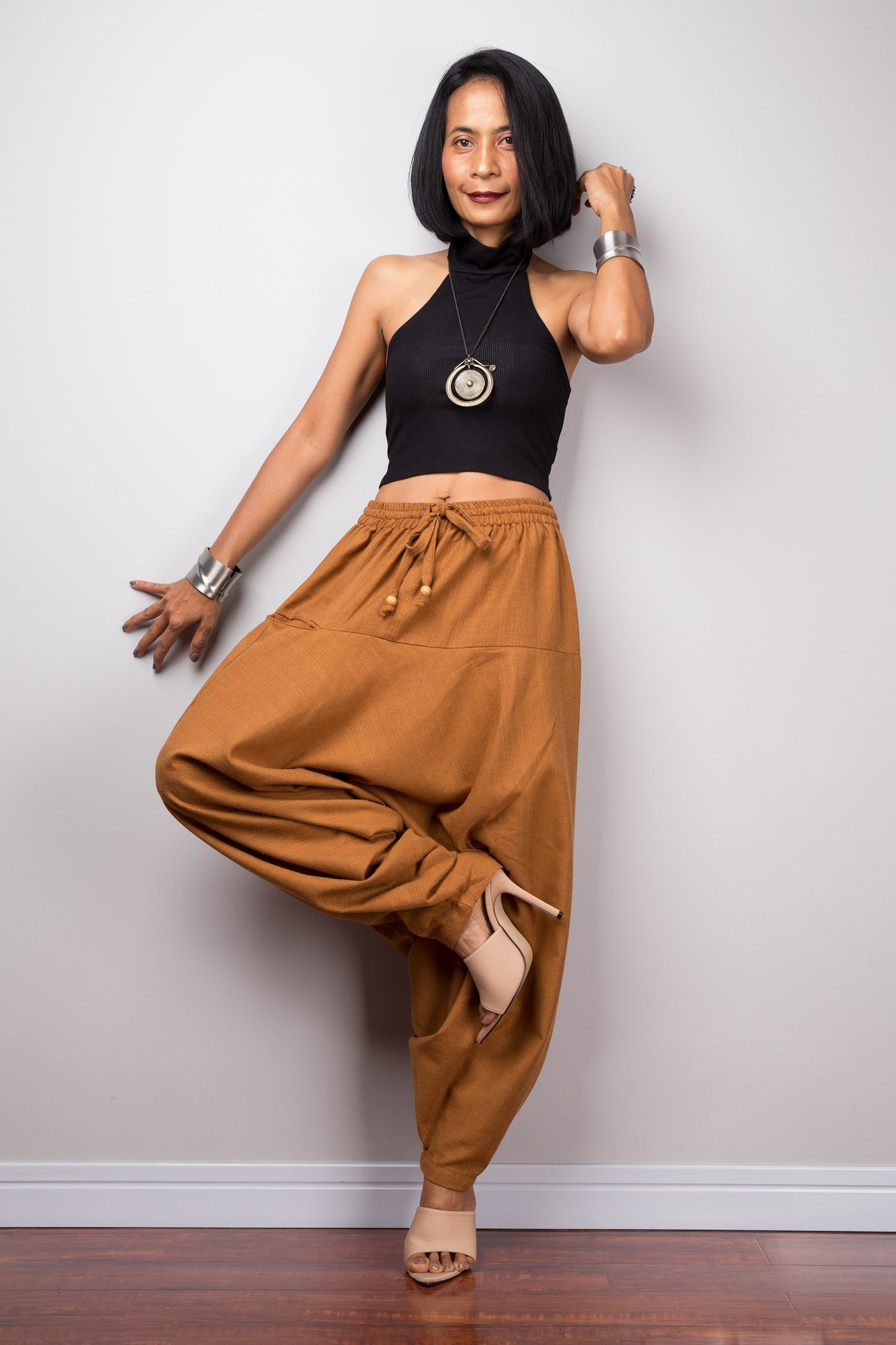 Model wearing brown harem pants with a loose fit, standing lotus pose against a plain background, showcasing the full-length view.