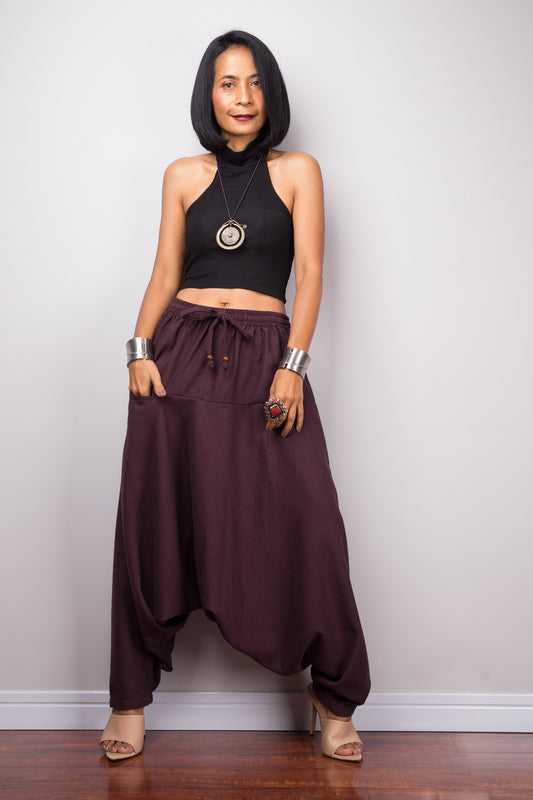 Model wearing burgundy harem pants with a loose fit, standing against a plain background, showcasing the full-length view and pockets.