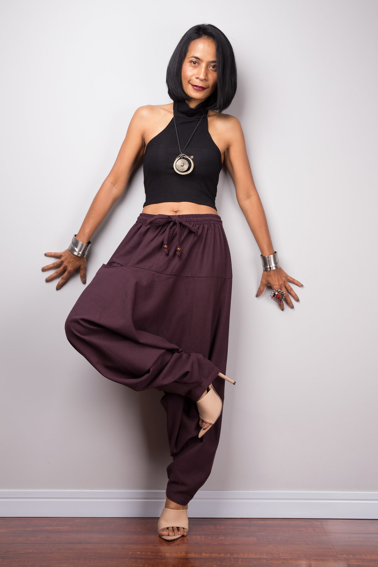 Model wearing burgundy harem pants with a loose fit, standing in lotus pose against a plain background, showcasing the full-length view.