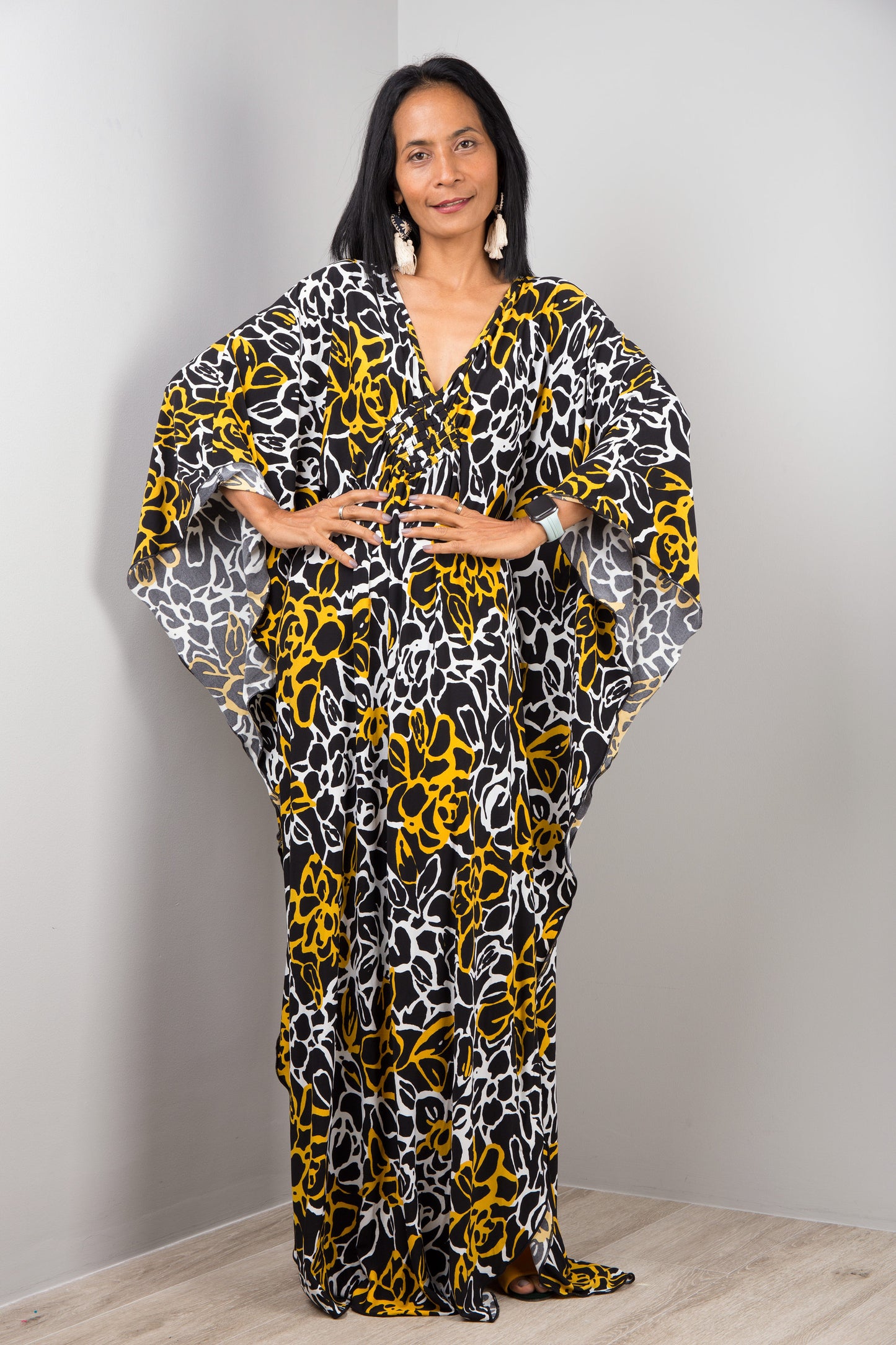 Nuichan’s black and yellow tie-dye kaftan dress with abstract floral designs, modeled by a woman with long black hair, posed gracefully in a minimalist studio with a gray background and light wood flooring.