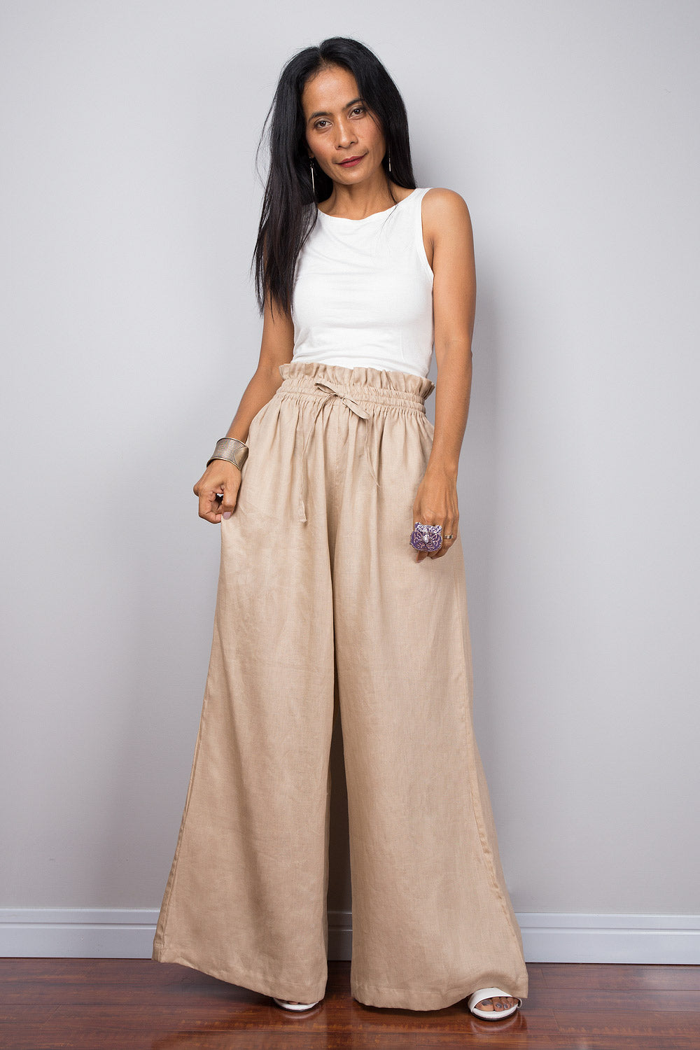 Front view of a woman modelling beige handmade natural linen palazzo pants with a high waist and wide legs, paired with a white top