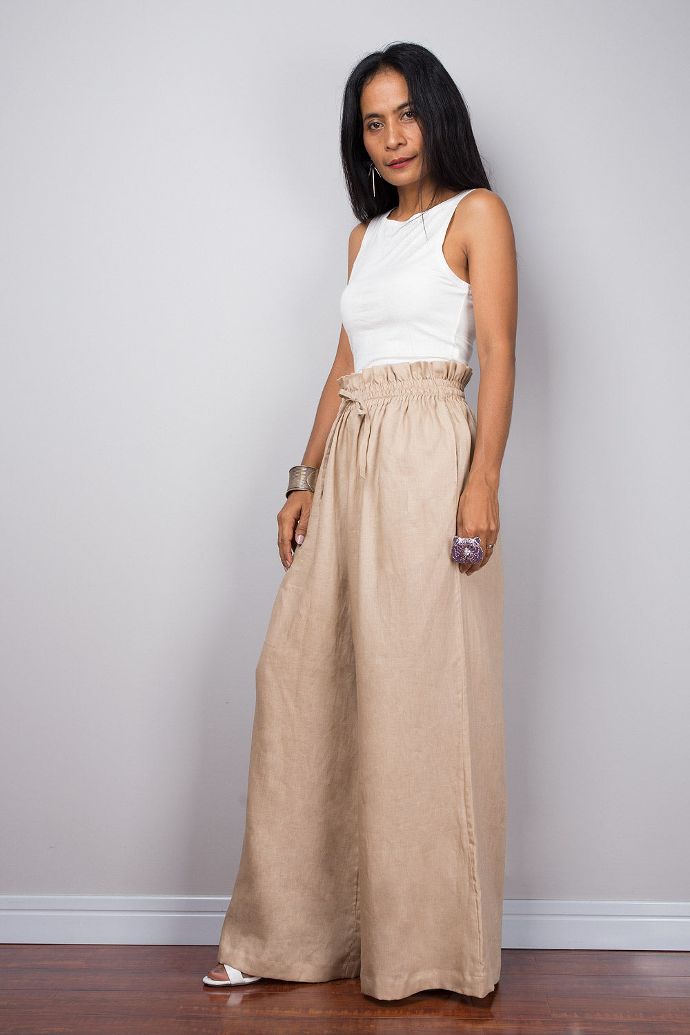 Lifestyle shot of a woman wearing beige linen palazzo pants with white sandals, ideal for a summer casual look.