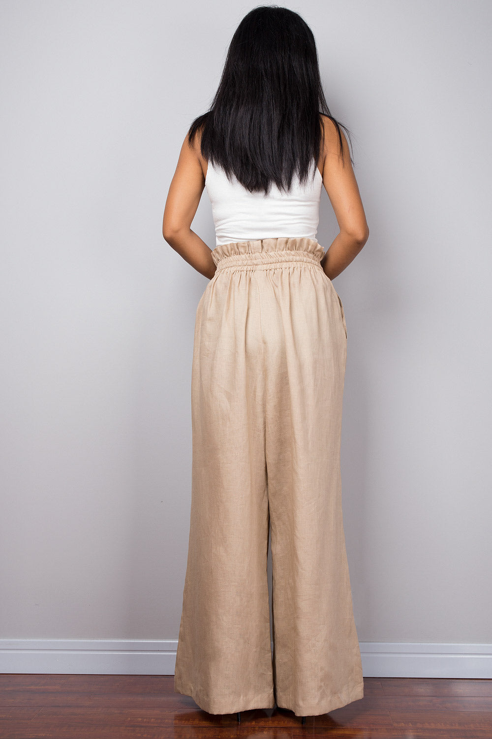 Back view of a woman wearing beige handmade linen palazzo pants, showcasing the high waist and flowing wide legs from behind