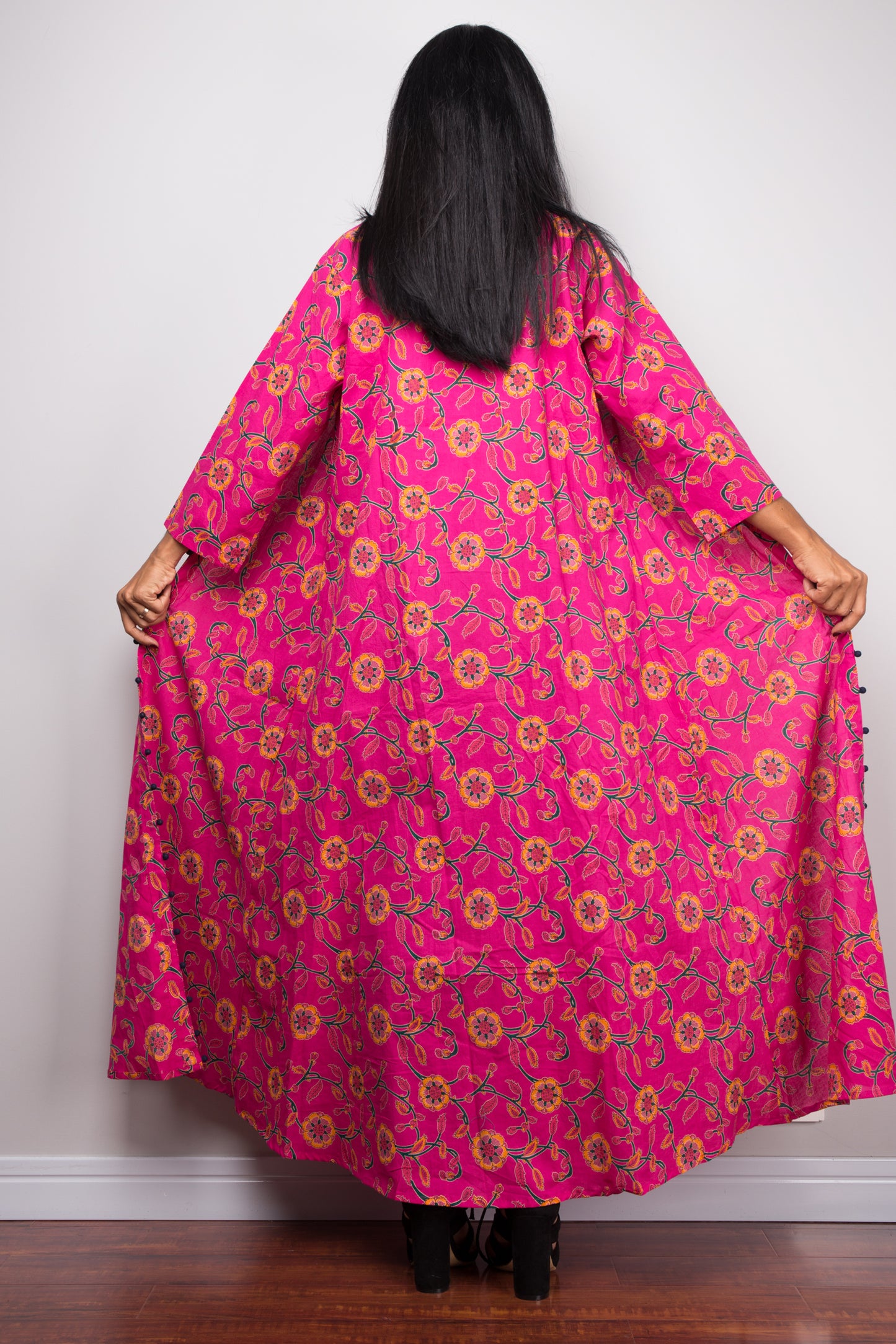 Detail of the floral pattern on a pink cotton open front cardigan, worn with a white crop top and blue jeans.