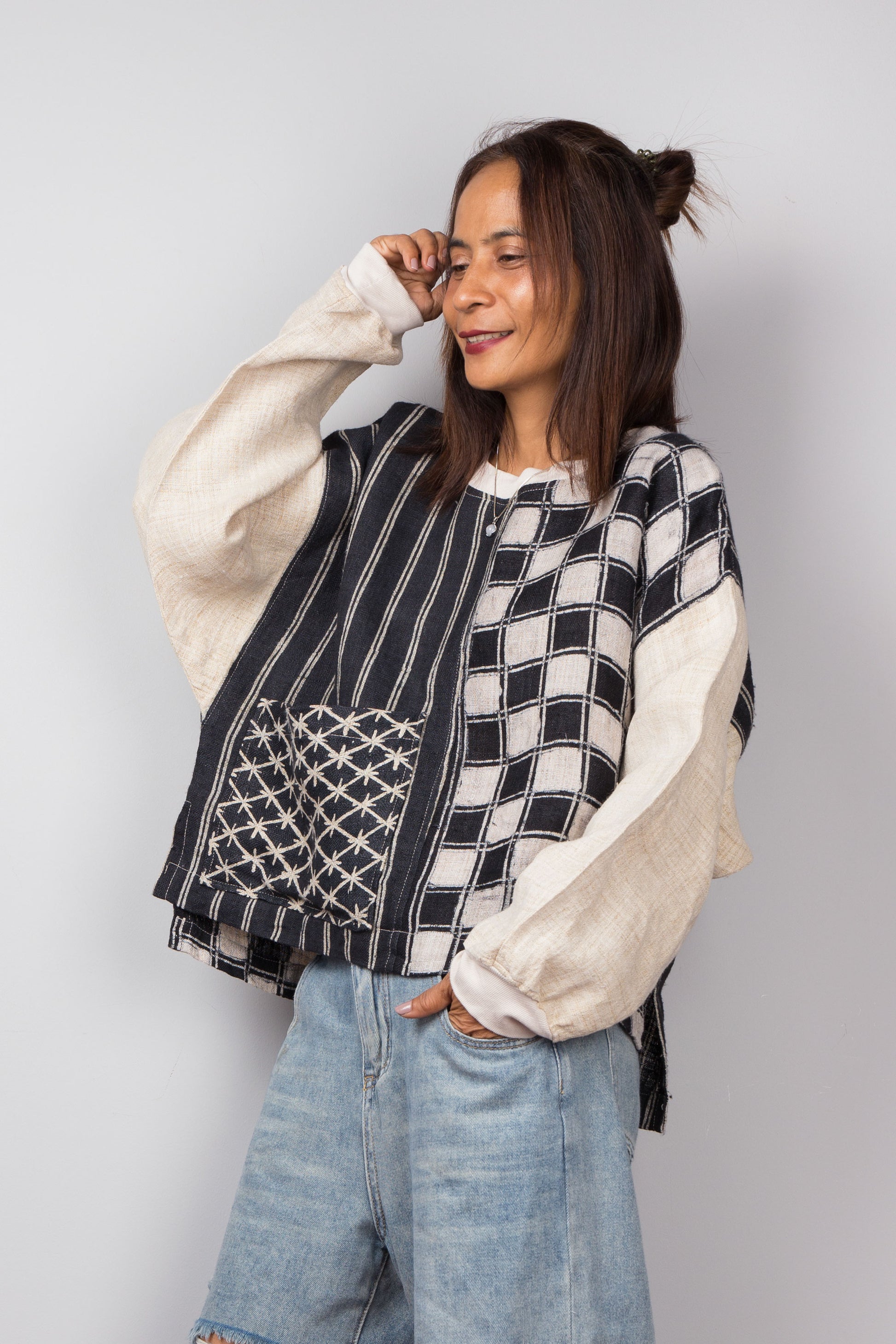 Handwoven hemp sweater with combination of a checkered and striped pattern. Two tone in black and off white. Model is holding up one arm. Long sleeve pullover top with crew neck