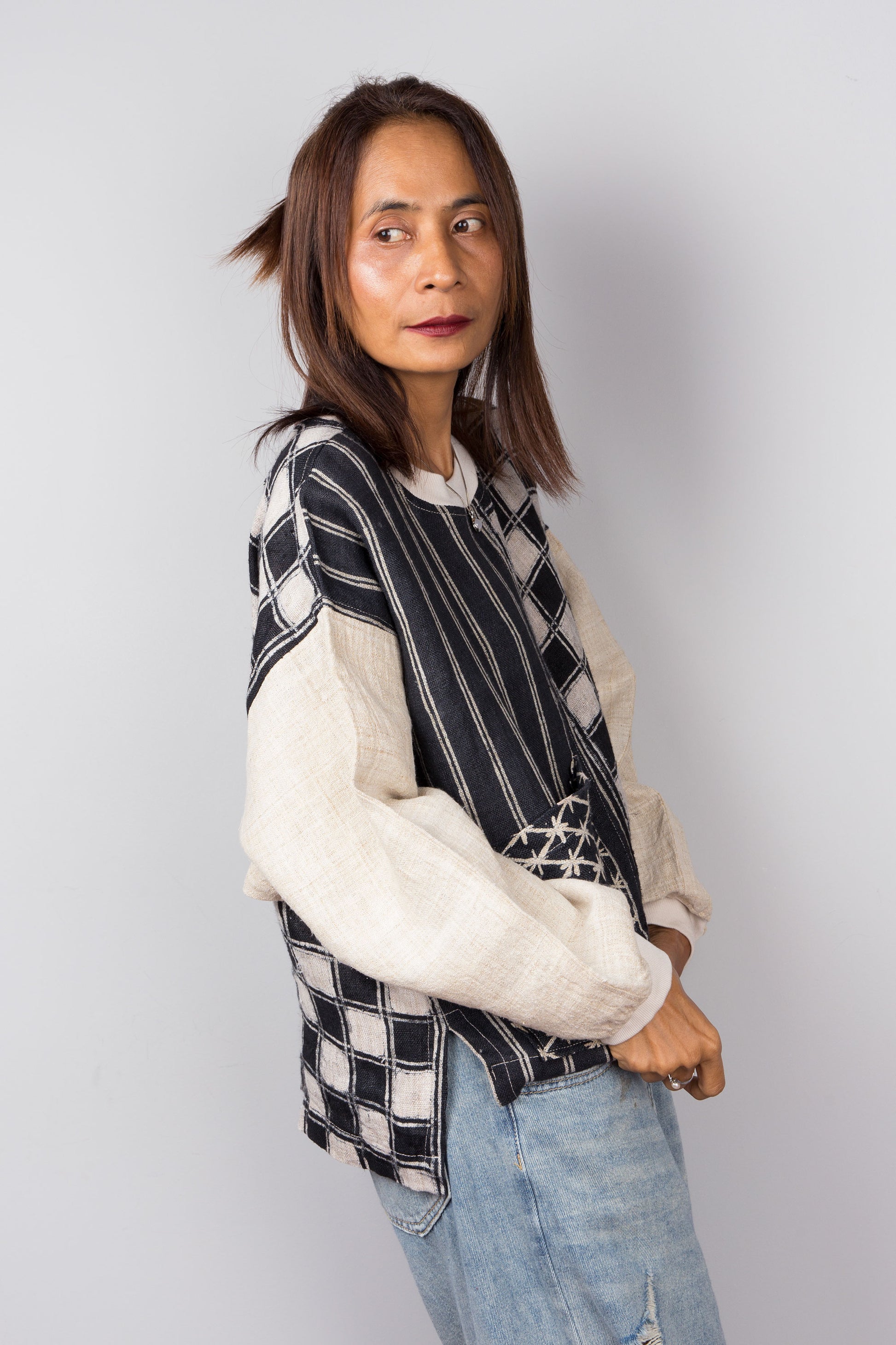 Handwoven hemp sweater with combination of a checkered and striped pattern. Two tone in black and off white. Side view. Long sleeve pullover top with crew neck