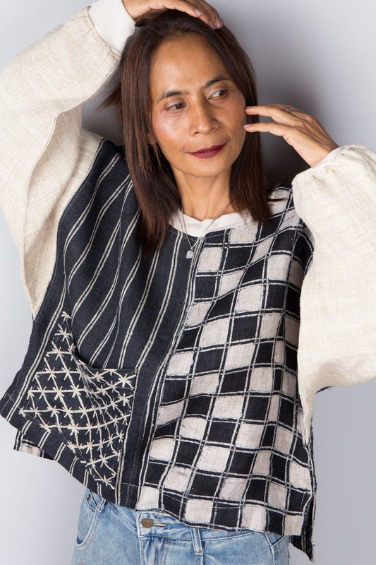 Handwoven hemp sweater with combination of a checkered and striped pattern. Two tone in black and off white. Model is holding up her arms. Long sleeve pullover top with crew neck