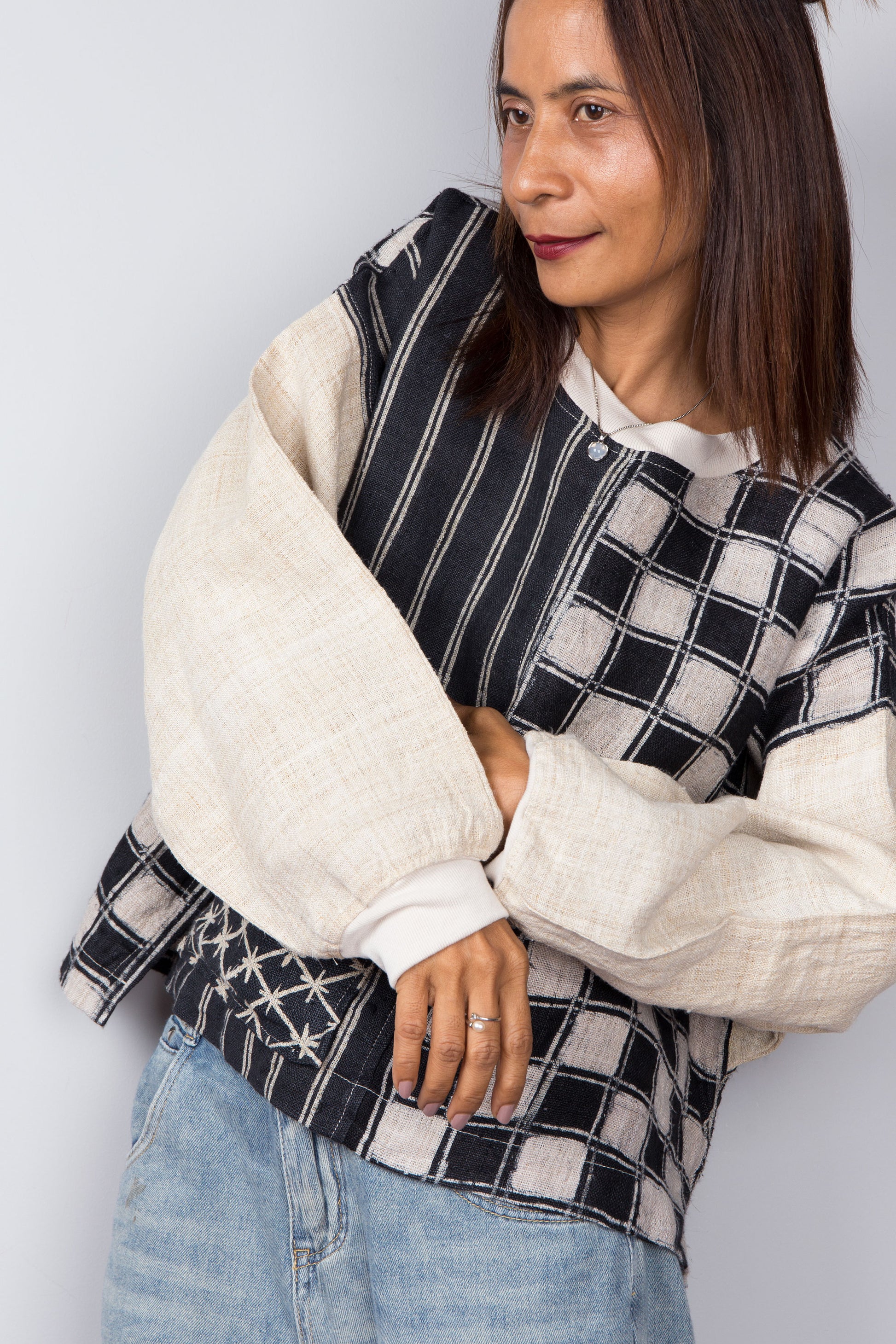 Handwoven hemp sweater with combination of a checkered and striped pattern. Two tone in black and off white. Close up view. Long sleeve pullover top with crew neck