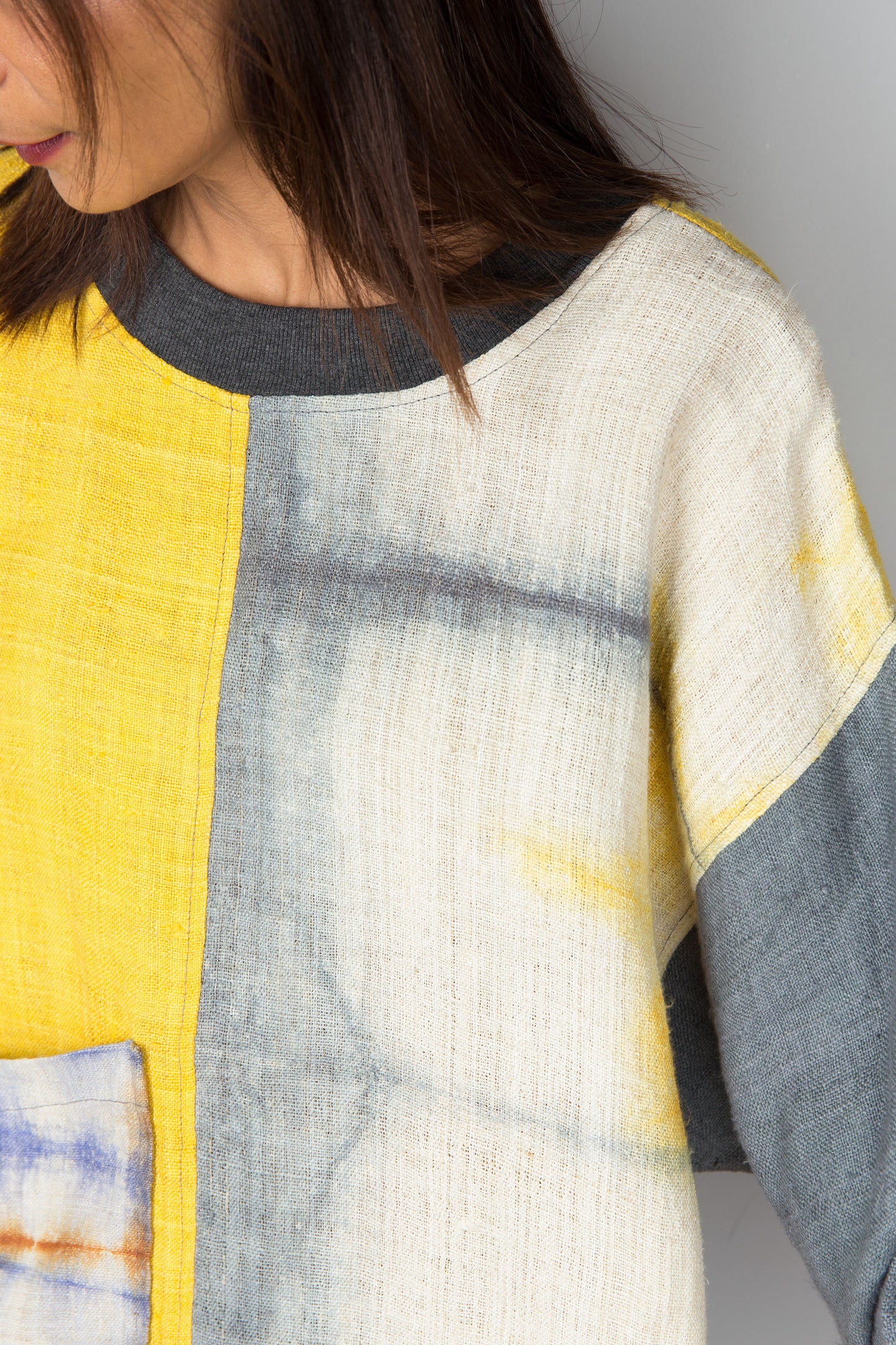 Hemp sweater in yellow and grey with shibori tie dye detail on the front pocket. Close up view.