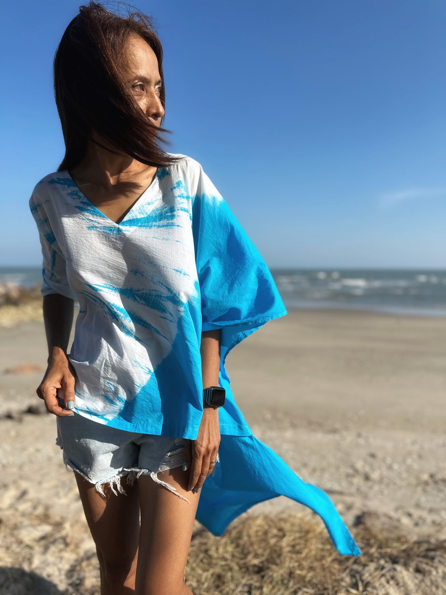 Front view of a short front kaftan dress in blue shibori tie dye, paired with distressed denim shorts, perfect for a day at the beach.