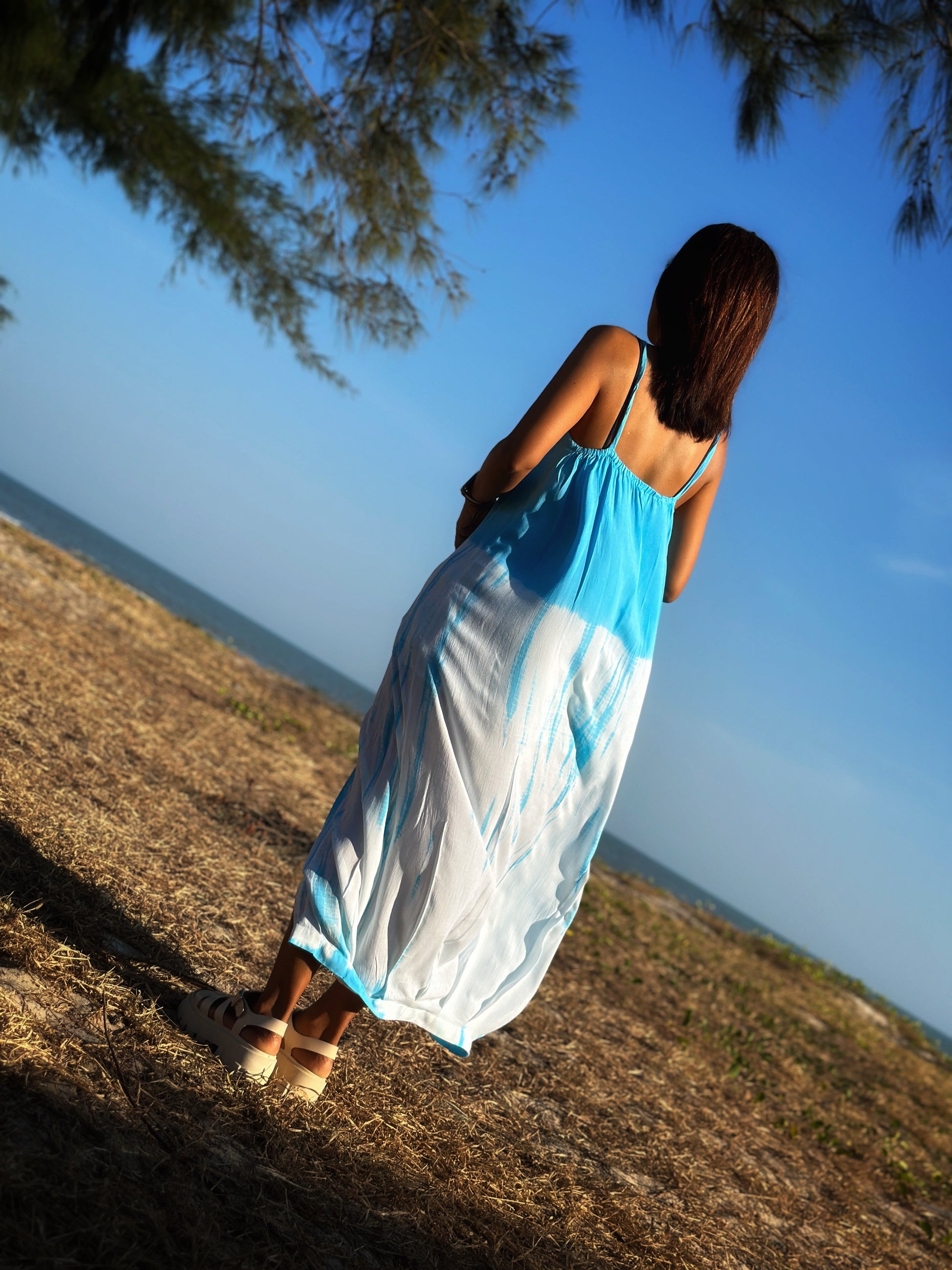 Model showcasing the elegant back of a light blue shibori tie dye dress, with delicate straps and a flowing split.