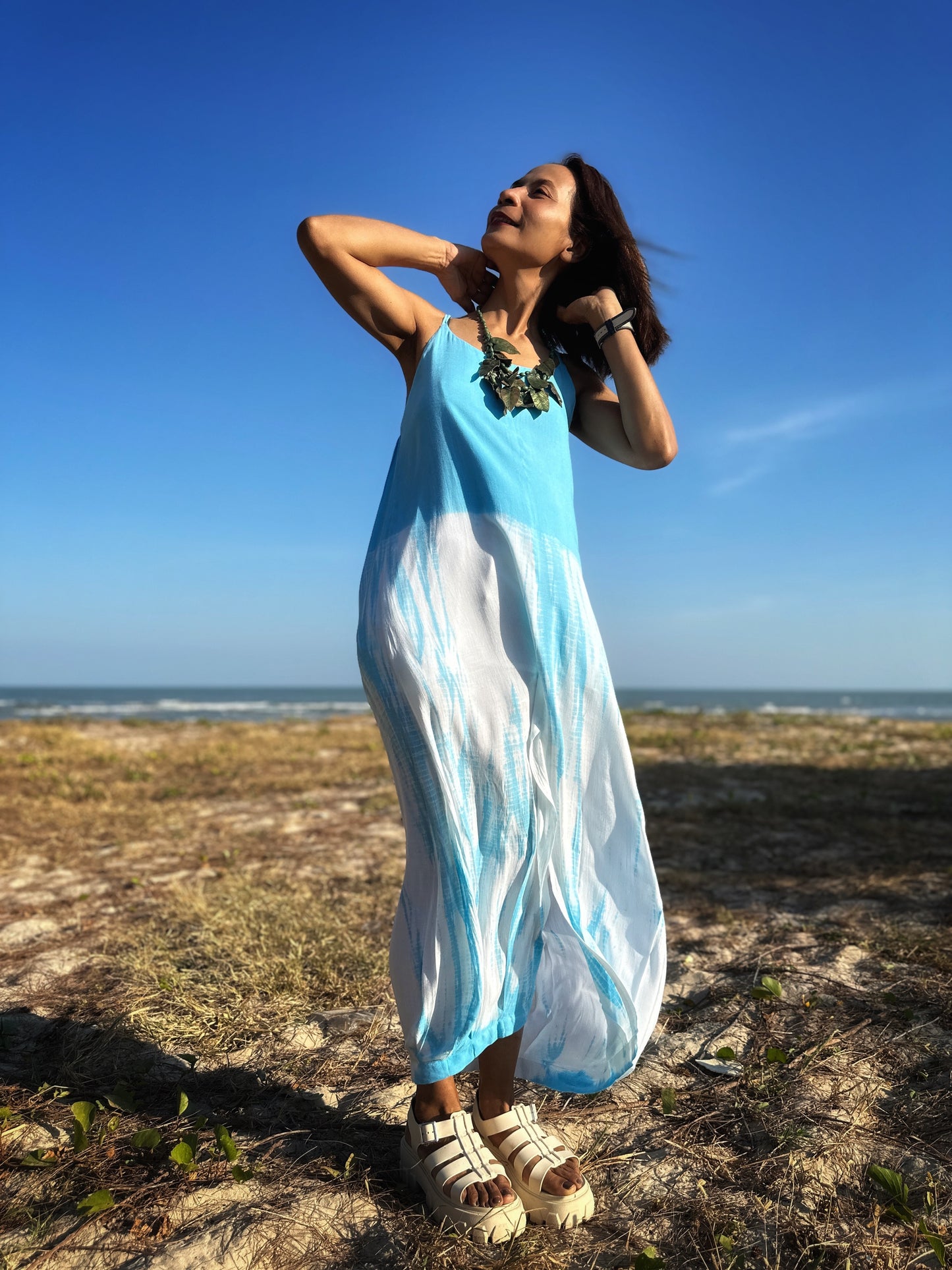 Woman in a light blue shibori tie dye strap dress with a stylish side split, posing gracefully on the beach