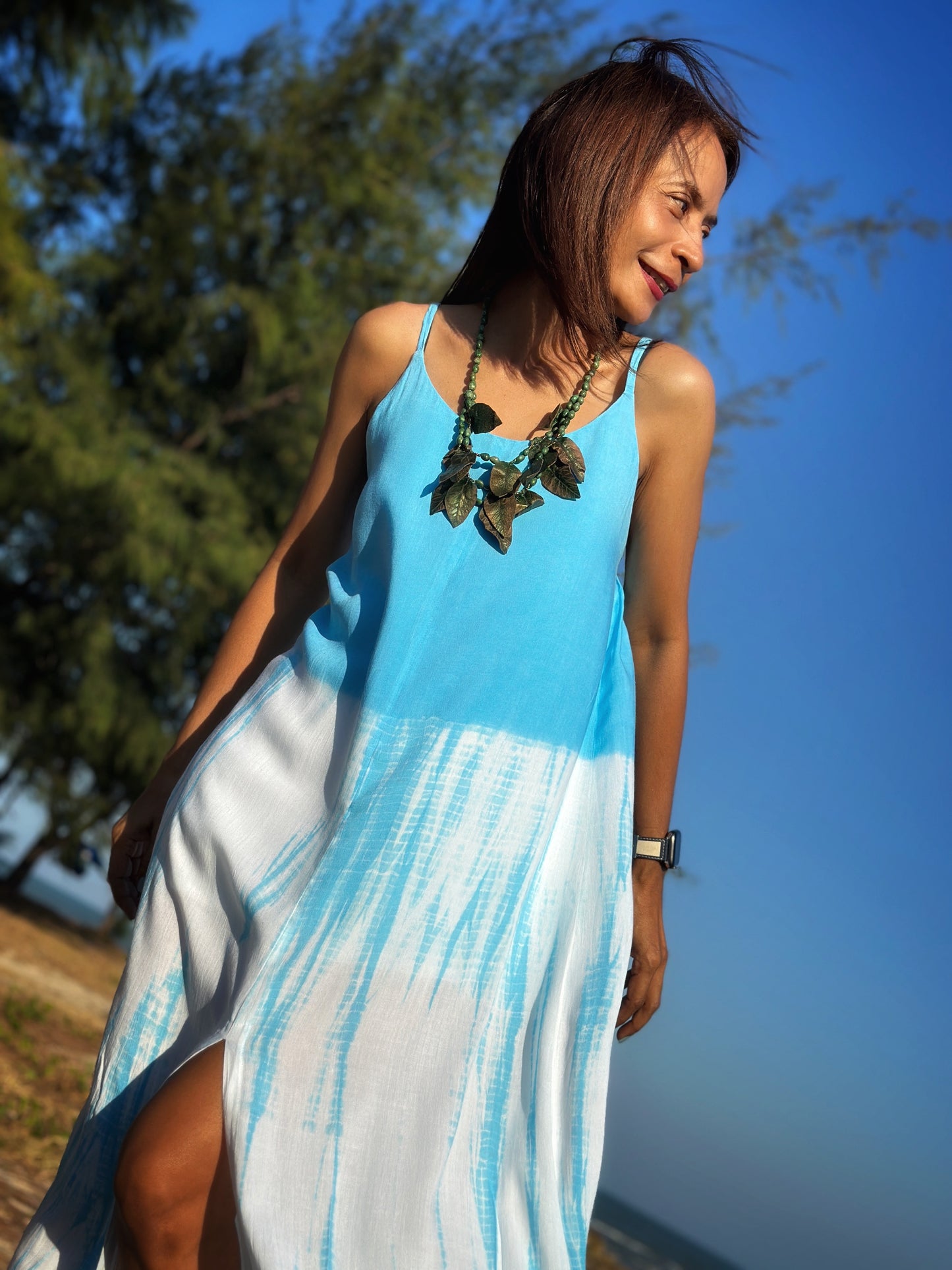 Woman in a light blue shibori tie dye strap dress with a stylish side split, posing gracefully