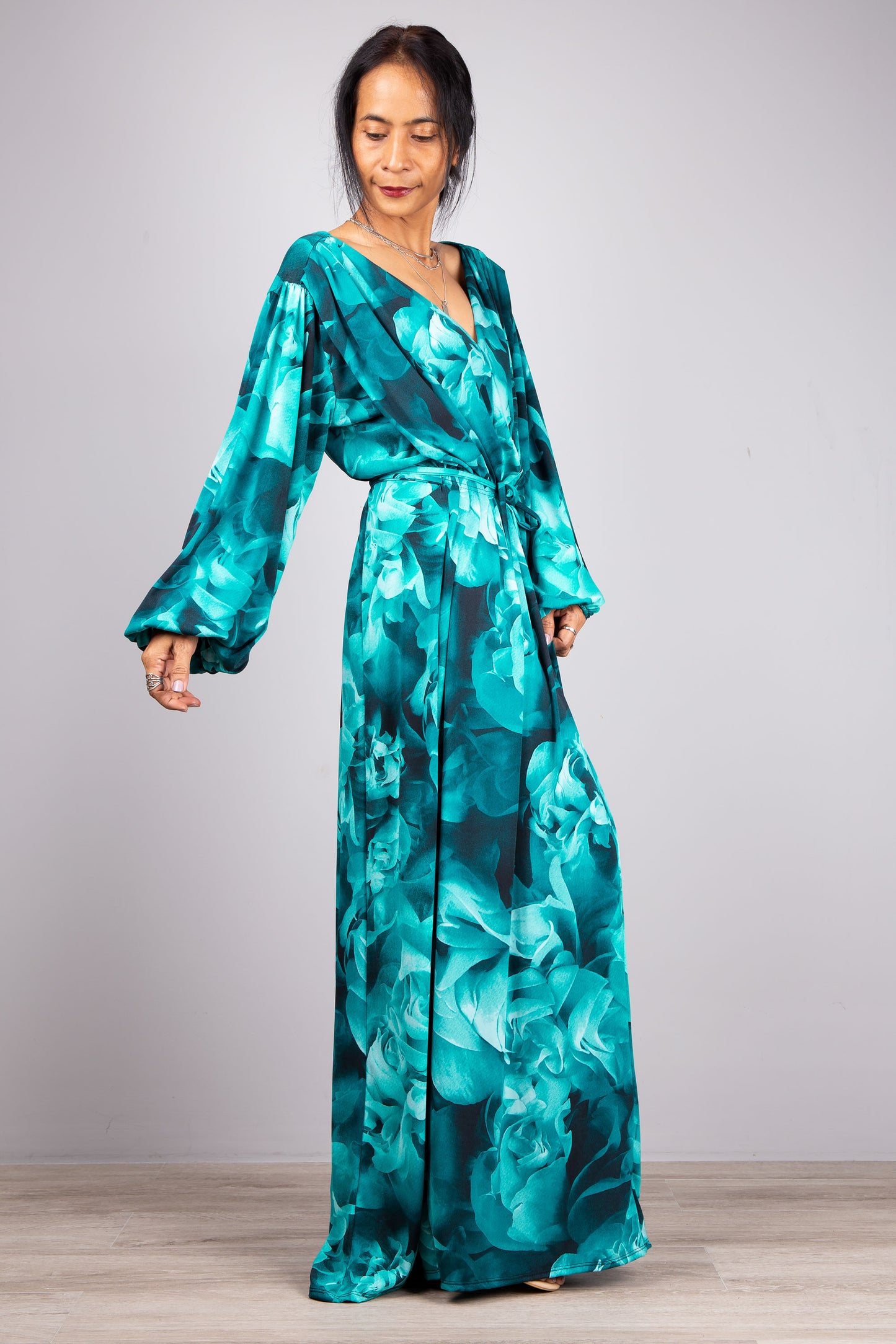 Turquoise Tide: The model stands gracefully in our Boho Chic Maxi Dress, the turquoise fabric flowing like water against the calm, light grey background.